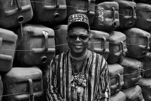 Black-and-white portrait of Romuald Hazoumè in front of his artwork