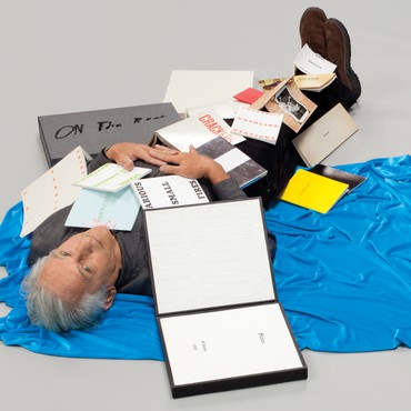 Ed Ruscha on the floor with his books scattered and open laying on top of him.