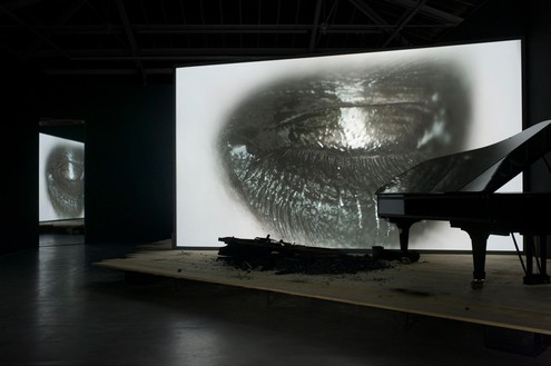 Douglas Gordon, Phantom, 2011 Video installation: a stage, a screen, a burnt Steinway piano, a black Steinway piano, and a monitor, dimensions variable, edition of 3© lost but found. Photo: Katharina Kiebacher