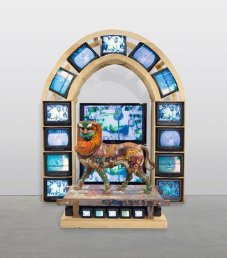 Painted wood lion sculpture standing on a wood base with TV monitors displaying color video below and behind it