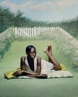 A black woman laying on her stomach on a blanket on grass surrounded by a white picket fence