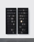 Artwork comprising two vertical black shelves filled with black porcelain pots and pieces of steel, tin, aluminum, and glass