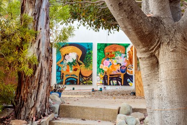 Two paintings leaning against a wall outside seen through trees