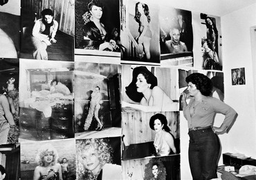 Black-and-white photograph of a woman looking at a wall filled with large photographs of people
