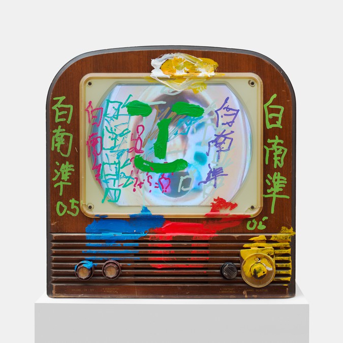 Wood vintage television with strokes of colorful paint applied to the exterior and over the screen, including Chinese characters