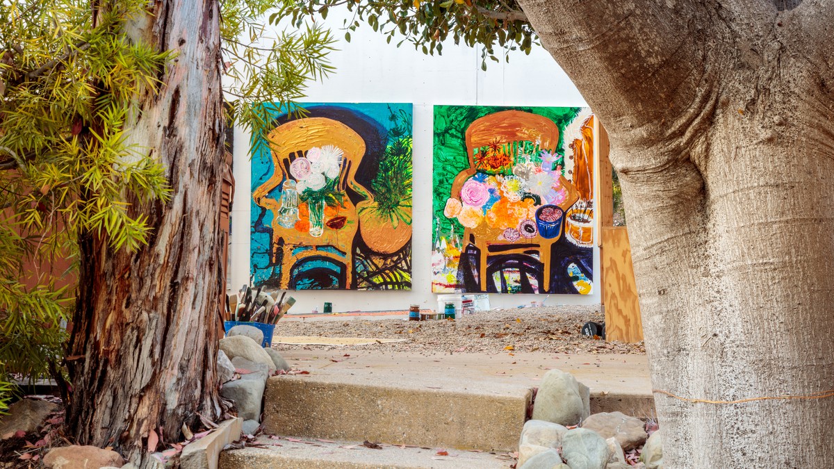 Two paintings leaning against a wall outside seen through trees