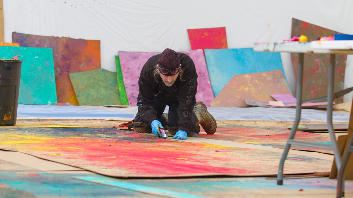 Sterling Ruby in his studio on his knee cutting painted cardboard