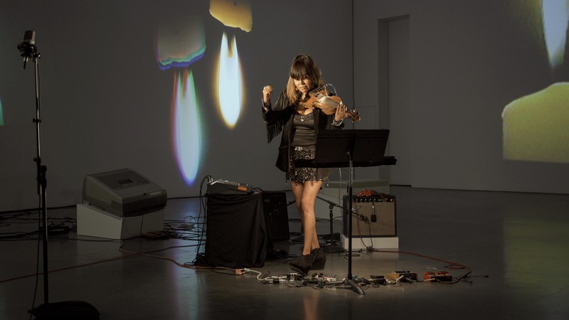 Laura Ortman playing a violin inside Art in Process: Part One a survey of works by Nam June Paik at Gagosian New York