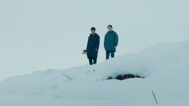 Two people stand on a snowy hill looking down