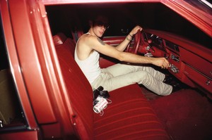 A person sits inside a red car, half of their face is in shadow