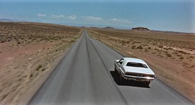 an open road in the desert with a single car driving on it