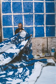 Portrait of Simon Hantaï holding on a blue and white canvas in his studio