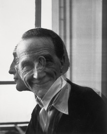 Double exposure of artist Marcel Duchamp, the first exposure showcases Duchamp looking out of the frame while the second exposure showcases Duchamp looking directly at the viewer and smiling