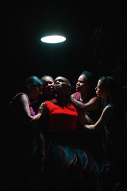 Five dancers huddle together under a white light