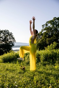 Dancer wearing a yellow bodysuit stands in a field with their arms raised to the sky