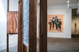 Installation view, Fashioning the Black Body, with wooden sculpture by Kenturah Davis in the foreground and colorful painting of four figures by Bisa Butler in the background.