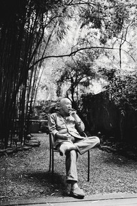 Black and white portrait of Chef Masa sitting on a chair while smoking a cigar