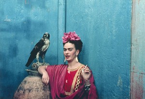 Frida Kahlo standing in front of a blue wall and wearing a magenta dress, she's smoking a cigarette next to an eagle