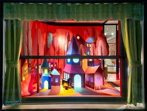 A window installation depicting a colorful village framed by olive green curtains