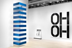 Installation of three pieces of art: stack of ten galvanized iron and blue plexiglass boxes afixed to the wall, black-and-white painting leaning against the wall, and black-and-white painting with the stenciled word "OH" twice, stack on top of each other