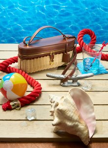 A bag, shell, beachball, and glass on a deck poolside