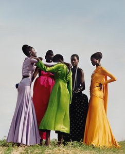 A group of black women standing in a semi-circle with bright colored dresses draping arms over each other