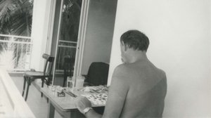 Cy Twombly sitting at a table outside with a drawing and drawing materials