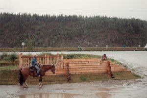A man on a horse and a man standing inside a wooden sculpture up against a tree covered mountainside