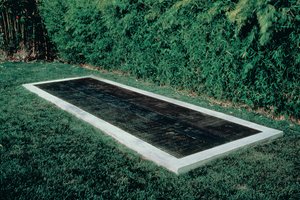 Rectangular shaped concrete pool surrounded by grass and hedges