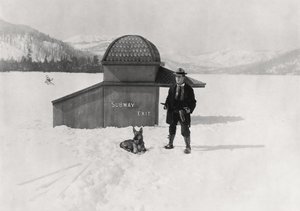 Man standing in the snow with a dog in front of a subway exit sculpture