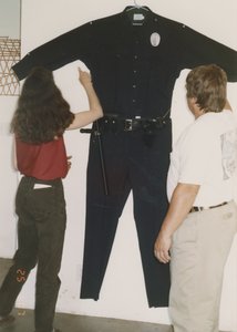 Two people inspecting a handmade copy of a police uniform hanging on the wall