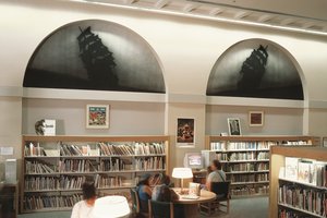 Library room with people around tables under two ship lunette paintings on the wall