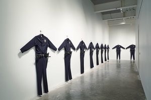 Gallery with ten oversize police uniform hanging in a visual cordon on the wall