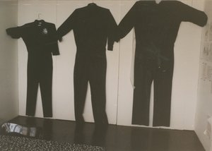 Three handmade police uniforms in varying sizes hanging on the wall